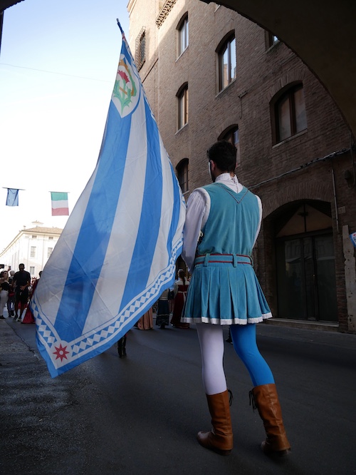 Uno sbandieratore vestito di bianco azzurro sotto al Torre dell'Orologio